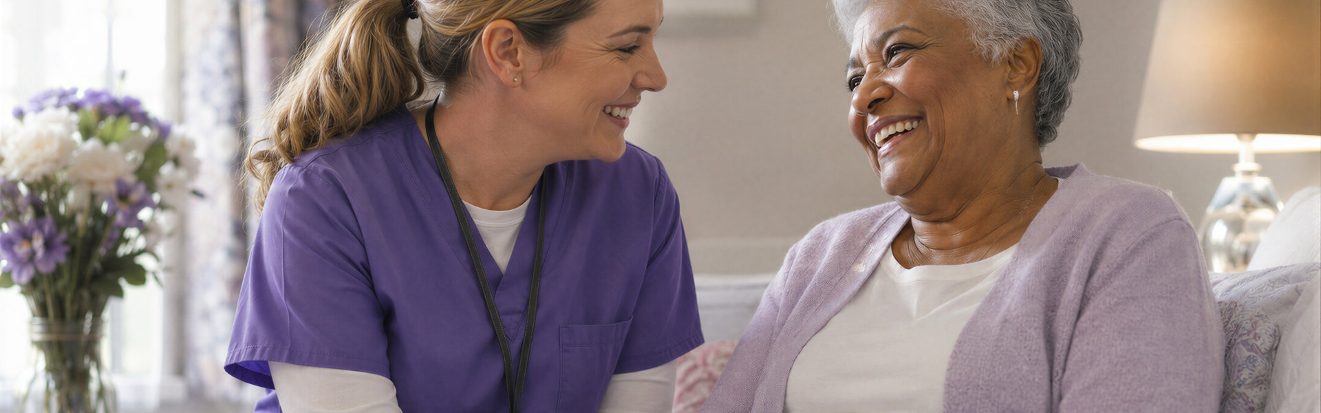 Female nurse in purple scrubs talking to a smiling elderly woman